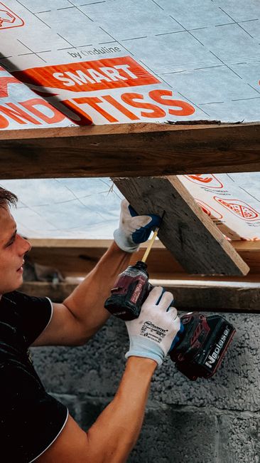 A homeowner examining attic insulation with a flashlight among wooden beams and pink fiberglass.