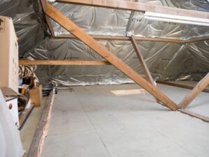 A homeowner inspecting aging insulation in an unfinished attic with a flashlight.