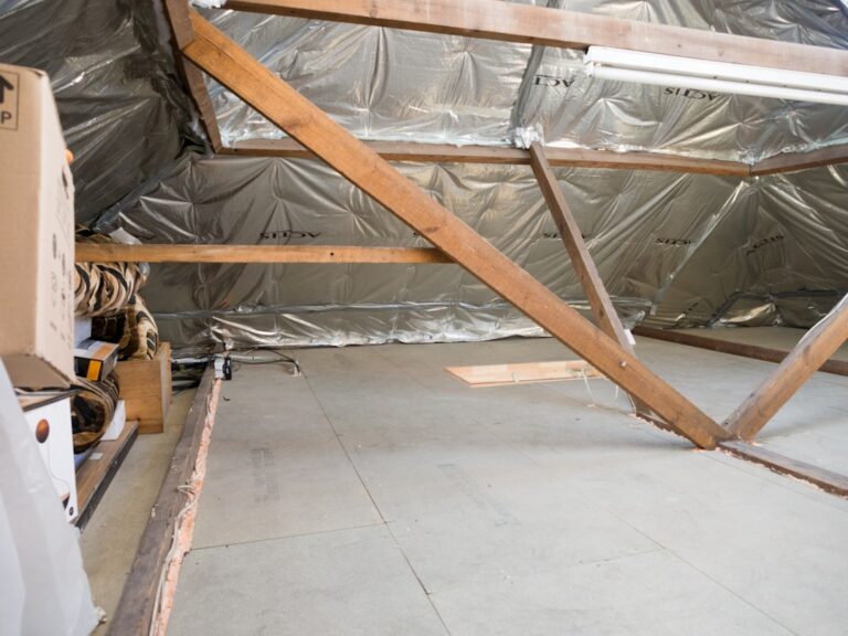 A homeowner inspecting aging insulation in an unfinished attic with a flashlight.